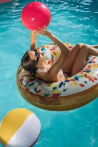 Frau sitzt in einem Poolring und wirft einen Wasserball in die Luft